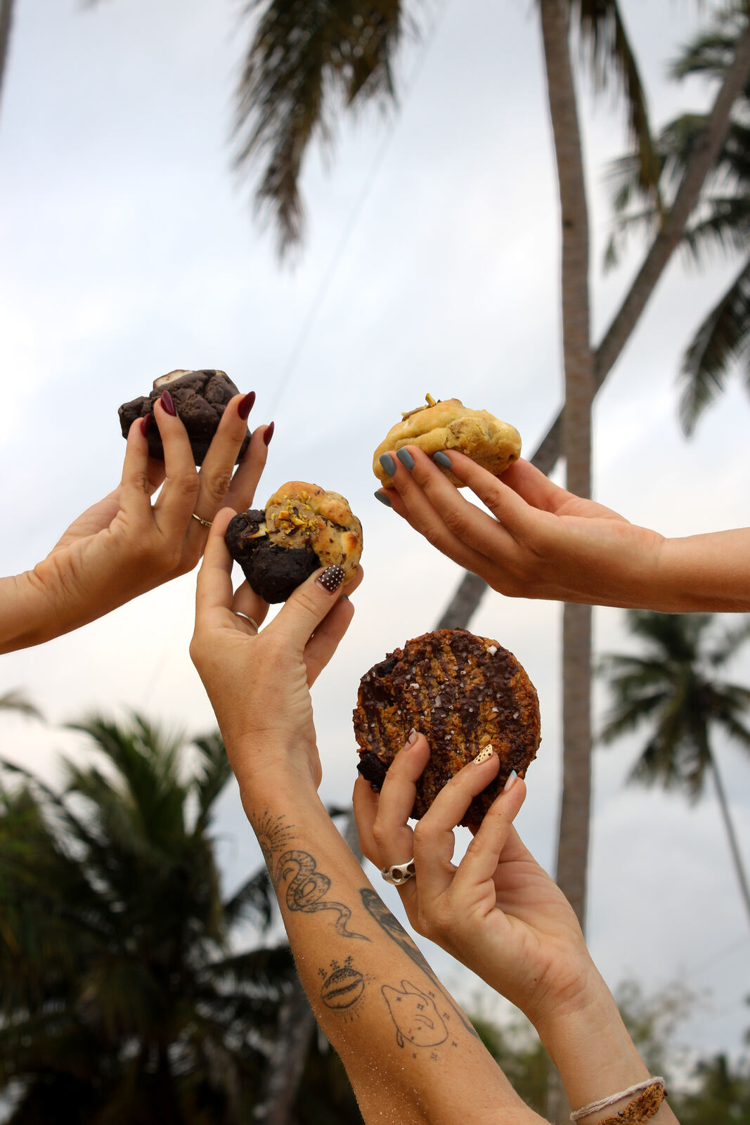 Hands holding Kookie cookies up under palm trees in Mirissa